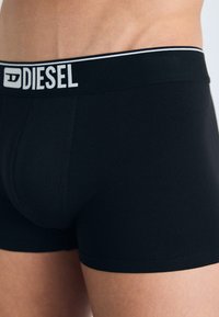Fekete pamut boxer alsónadrág fehér Diesel logóval a rugalmas derékrészen. Sima textúra, testhez álló kialakítás és térd közepéig érő hosszúság.