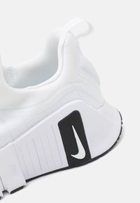 White athletic shoe with a textured upper, featuring a black rubber accent with a white Nike logo, and a pull tab at the heel.