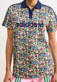 Blommönstrad polo med marin krage och ärmar med tre ränder. Har en broderad Adidas-logga i marin. Mjuk tygkvalitet, livfulla färger.