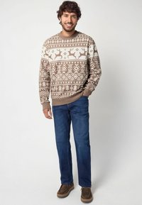 Bruine gebreide trui met witte rendieren en geometrische patronen; geribbelde manchetten en zoom; gecombineerd met blauwe jeans en bruine schoenen.