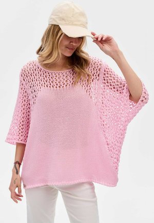 Rosa gestrickter übergroßer Pullover mit einem lockeren, offenen Gewebe-Design, weiten Ärmeln und rundem Ausschnitt, kombiniert mit einer beigen Mütze.