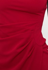 Punainen mekankangas, jossa on kerättyjä laskoksia ja sivussa kaareva ommelseura.