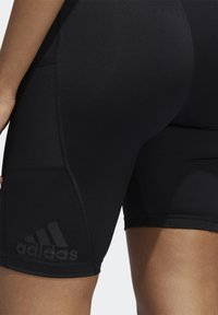 Shorts de sport noirs en matière extensible, présentant une texture lisse et un logo adidas bien visible sur la cuisse gauche en noir.