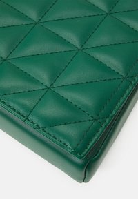 Zelený kožený povrch s prošívaným trojúhelníkovým švem, který vytváří geometrický vzor, zobrazující detaily rohů a okrajů.