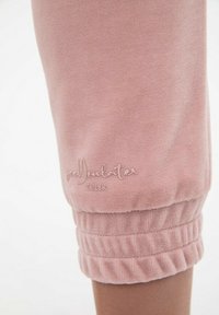 Jasnoróżowe dresy z prążkowanymi ściągaczami i miękką teksturą. Na dolnej części nogawki haftowany napis "goJULATER CUL8R".