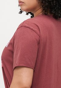 Maroon short-sleeve T-shirt made of soft fabric, featuring a round neckline and casual fit. Visible stitching along the sleeve edges.