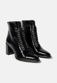 Botine negre din piele lacuită, cu vârful ascuțit, finisaj texturat, fermoar lateral și șireturi decorative cu accente metalice în față.