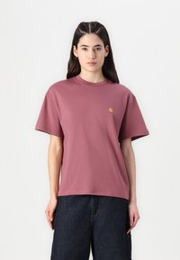 Mörkröd bomullströja med korta ärmar, lös passform och en liten gul logotyp på bröstet. Bärs tillsammans med mörka jeans.