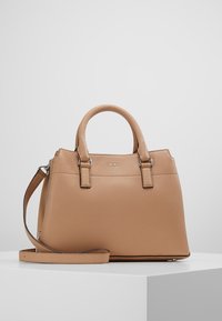 Beige läderhandväska med strukturerad yta, dubbla korta handtag, avtagbar axelrem och subtil logotypdetalj på framsidan.