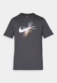 Šedé krátké tričko z bavlny s krátkým rukávem, na kterém je velké bílé logo Nike swoosh s barevnými tečkovanými vzory a textem níže.