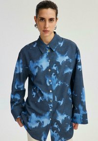 Camicia oversize blu scuro con bottoni, caratterizzata da un motivo astratto blu chiaro, maniche lunghe e colletto classico in tessuto intrecciato.