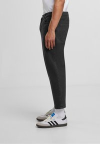 Mustat farkut slim fit -mallissa, viisi taskua, ommeltu yksityiskohtia, käytetään valkoisten urheilukenkien ja nilkkasukkien kanssa.