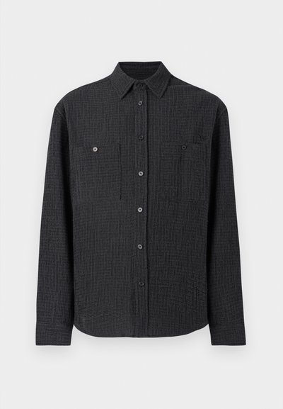 Μαύρο πουκάμισο με κουμπιά, φτιαγμένο από υφή υφάσματος, με δύο τσέπες στο στήθος και κωνικό γιακά. Μακριά μανίκια με κουμπιά στους καρπούς.