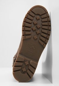 Suela de goma marrón con patrón de textura. Presenta un logo circular, tamaño 37, y bordes suaves con un talón ligeramente redondeado.