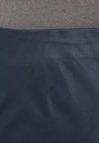 Tumši zila auduma ar gludu tekstūru, apvienota ar pelēku adītu audumu augšpusē. Raksturīgs tīrs dizains bez apdares elementiem.