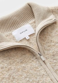 Beige knitted sweater with a textured surface; features a silver zipper and a ribbed collar. Label reads "OPUS," size 36.