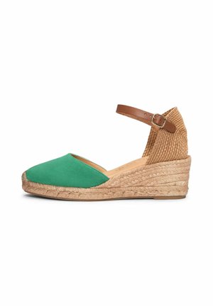 Zapato cuña espadrille verde con suela trenzada de yute, tacón tejido y correa marrón en el tobillo con cierre de hebilla.