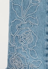 Broderie florale blanche avec des roses et des feuilles sur un tissu en denim bleu clair.