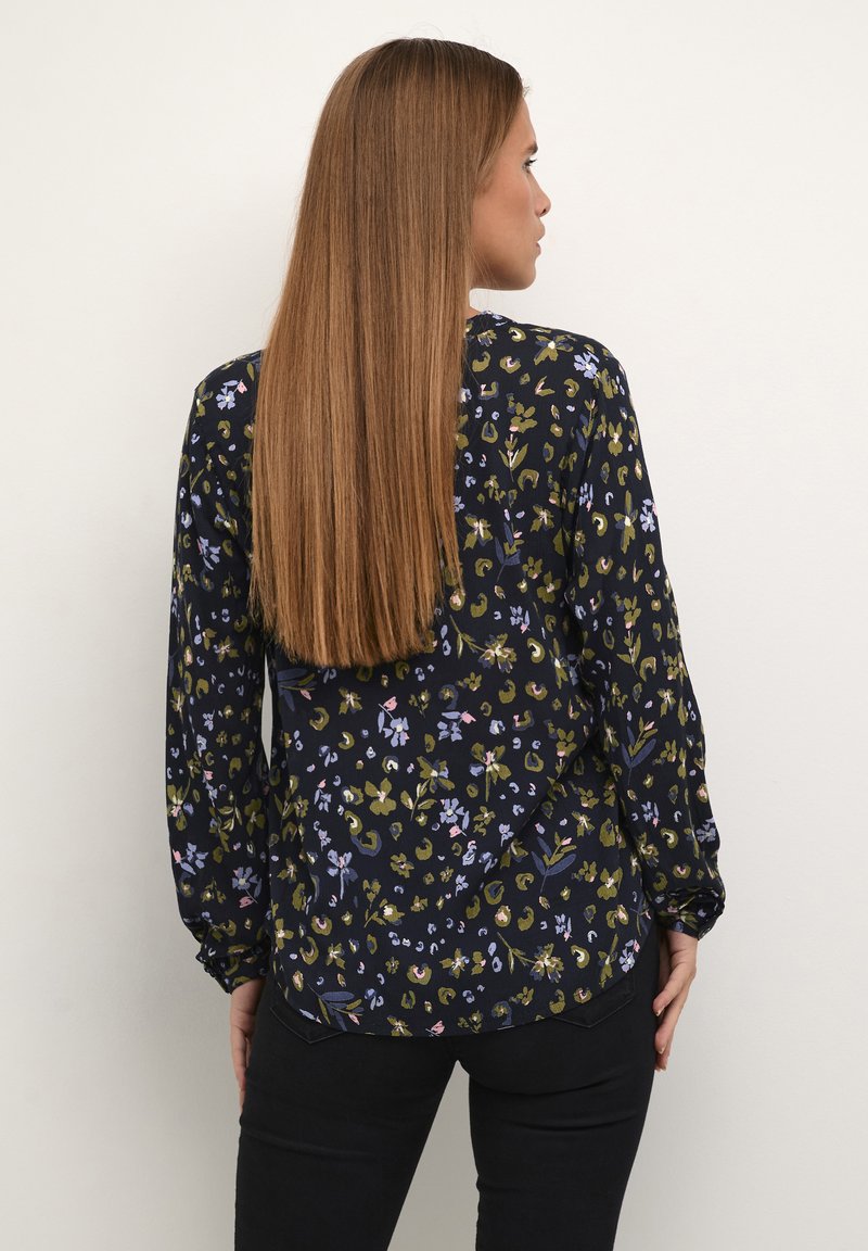 Blusa a maniche lunghe di colore blu navy con motivi floreali in verde, blu e rosa; presenta una vestibilità rilassata e un orlo arrotondato.