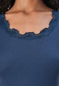 Top canelado azul-marinho com decote em renda preta scalloped, apresentando uma textura suave e um design ajustado.