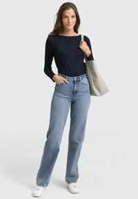 Marineblauwe longsleeve top, lichtblauwe hoge taille jeans en witte sneakers; met een grijze schoudertas. Glad materiaal, ruime pasvorm, klassiek ontwerp.