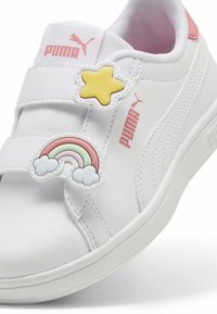 Hvit sneaker med borrelåsremmer, gummisåle, gul stjerne og regnbue detalj. Har rosa detaljer og en teksturert overflate. PUMA-merke inkludert.