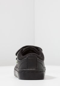 Černé tenisky s hladkým koženým svrškem, kulatou špičkou, polstrovaným límcem a texturovanou gumovou podrážkou. Obsahují decentní logo a minimalistický design.