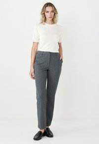 Grau gestreifte Hose mit taillierter Passform, ausgestattet mit vorderen Taschen und einer glatten Textur, kombiniert mit einem kurzärmeligen cremefarbenen Oberteil.