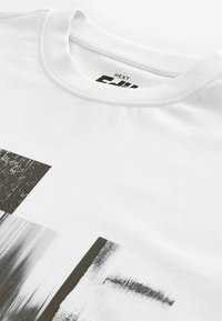 White cotton T-shirt featuring a black and gray abstract graphic print with varying textures. Round neckline and standard fit.