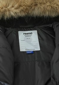 Czarna pikowana kurtka od wewnątrz z miękkim, beżowym kapturem wyłożonym futrem, metka z informacjami o pielęgnacji oraz oznaczenie produktu bluesign®. Metka wskazuje "reima" oraz rozmiar 92/2T.
