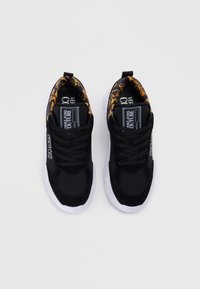 Sorte sneakers med teksturert overdel, med svarte lisser og hvit såle. Innvendig har de et gullfarget blomsterdesign. Logo synlig på siden.