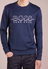 Marinblå sweatshirt med en vit logotyp "BOSS HUGO BOSS", rund hals, ribbade muddar och en mjuk bomullstextur. Enkel design, avslappnad passform.