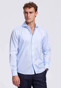 Lichtblauw overhemd met lange mouwen van gladde stof, met een klassieke kraag en knoopsluiting aan de voorkant met een subtiele glans, gestoken in donkere broek.