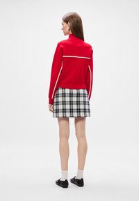 Sudadera roja con ribetes blancos, combinada con una falda de cuadros en blanco y negro. El conjunto presenta un diseño deportivo y un ajuste casual.