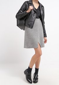 Veste de moto en cuir noir, blouse noire, jupe grise avec fente avant, et bottines noires avec accents de boucle. Stylé avec des chaussettes noires.