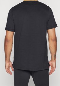 Černé tričko s krátkým rukávem a kulatým výstřihem, se shrnovanými manžetami a bočními rozparky. Vyrobeno z hladké bavlněné tkaniny. Bez viditelných vzorů.