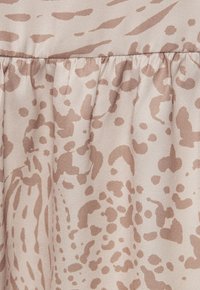 Peščena tkanina z subtilnim vzorcem živali, ki ima različne odtenke rjave barve in zbrano teksturo ob robu.