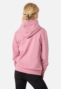 Rosa hoodie med avslappnad passform, som har en rymlig huva och ribbade muddar. Tyget verkar mjukt och slätt, vilket framhäver komfort.