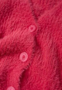 Chlupatý růžový cardigan s měkkou texturou a pěti lesklými růžovými knoflíky na přední straně, které zdůrazňují jeho pletený design.