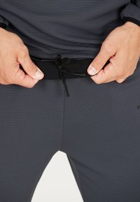 Dunkelgraue Sporthose mit strukturiertem Stoff, elastischem Bund mit schwarzen Kordeln und dezentem Markenlogo an der Seite.