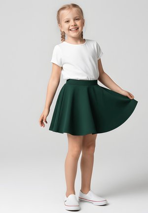 Biała bluzka z krótkim rękawem w połączeniu z zieloną rozkloszowaną spódnicą. Spódnica ma gładką fakturę i szeroki pas, uzupełniona białymi wsuwanymi butami.