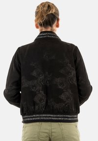 Veste bomber noire avec un motif léopard texturé, col côtelé et ourlet rehaussé de détails argentés. Comprend des poignets et un taille élastiques.