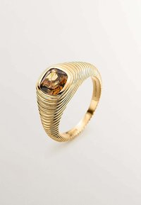 Anillo de oro con una banda texturizada y ondulada, que presenta una piedra preciosa marrón facetada engastada en un bisel cuadrado en la parte superior.