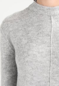 Maglione grigio a maglia con collo alto e bordi a costine, caratterizzato da una texture morbida e dettagli di cucitura minimi sul davanti.