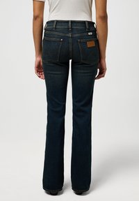 Dark blue flared jeans made of denim, featuring a high waist, stitched back pockets with chevron detailing, and a leather brand patch.