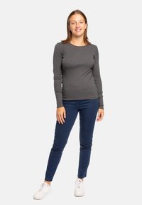 Maglietta grigia a maniche lunghe con silhouette aderente, abbinata a jeans skinny blu e sneakers bianche. Tessuto liscio con scollo a girocollo.