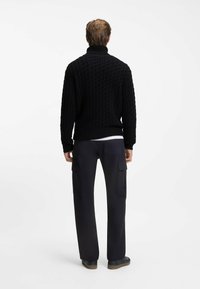 Schwarzer, kabelgestrickter Rollkragenpullover mit geripptem Saum, kombiniert mit dunklen Cargo-Hosen mit Seitentaschen und einem entspannten Schnitt.