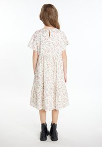 Blumendruckkleid mit kurzen Flatterärmeln, gerafftem Taillenteil und gestuftem Rock. Mit einem Schlitz am Rücken. Kombiniert mit schwarzen Knöchelstiefeln.