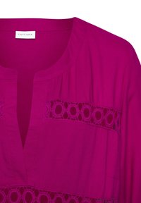 Blusa fucsia con escote en V y detalle de encaje circular en el pecho. Fabricada en una tela suave con textura lisa.
