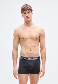 Γκρι ανδρικά εσώρουχα μποξεράκια με μαύρη ελαστική μέση που φέρει την επιγραφή «JACK & JONES» σε λευκό κείμενο. Το ύφασμα φαίνεται μαλακό και απαλό.